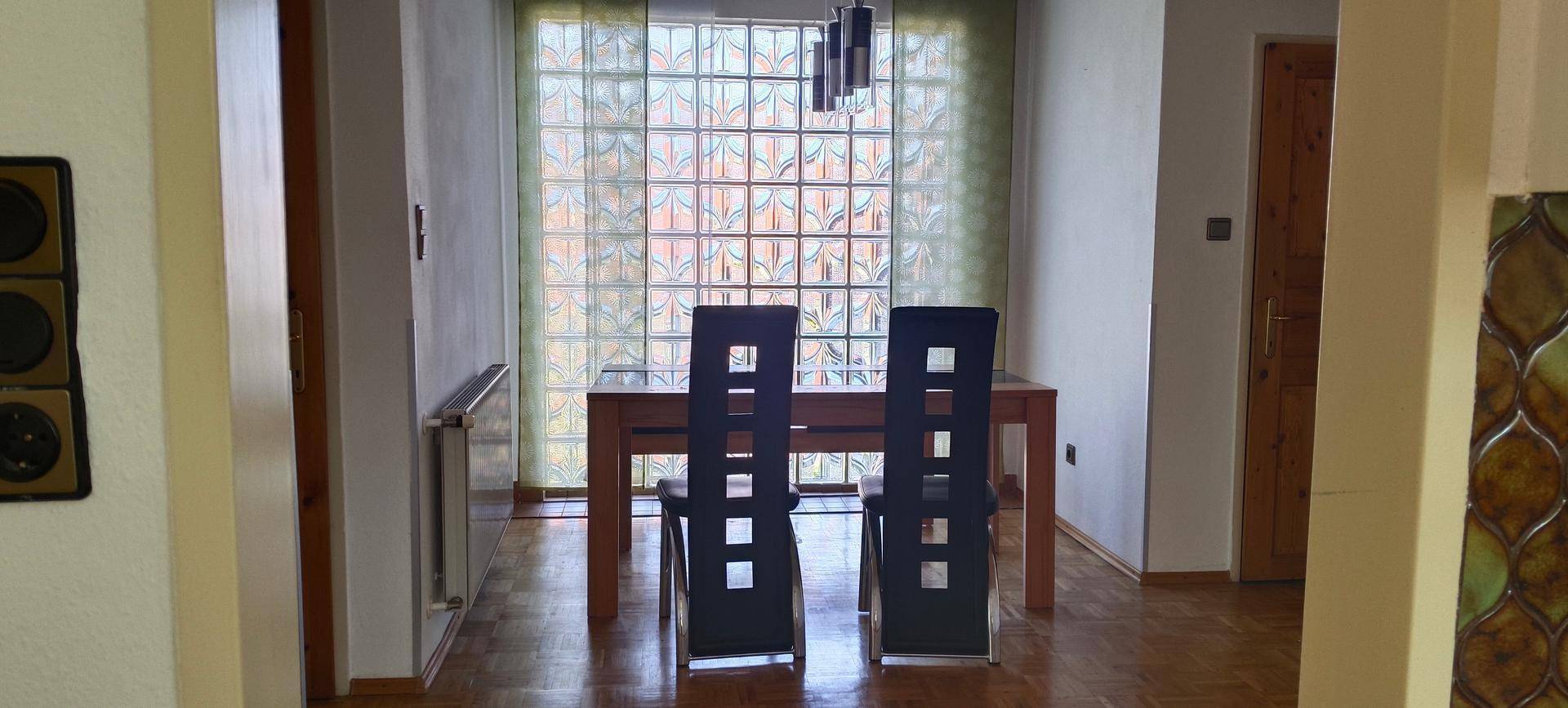 Essbereich mit Holztisch, modernen Stühlen und einer dekorativen Glasbausteinwand.
