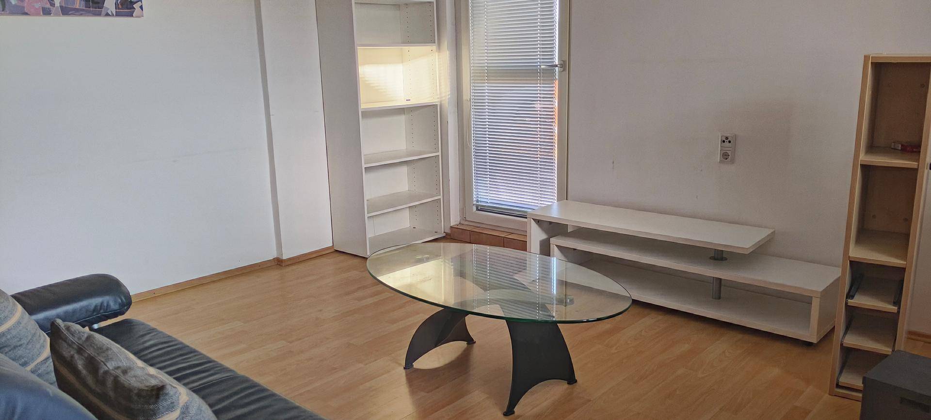 Wohnzimmer mit hellen Wänden, Holzfußboden und modernen Regalen sowie einem Glastisch.