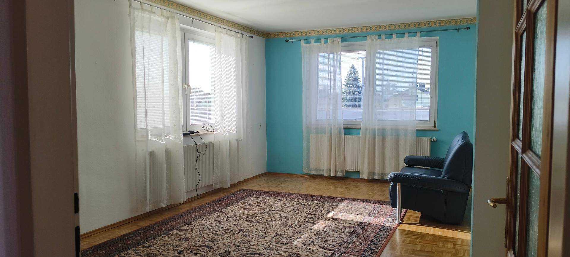 Helles Wohnzimmer mit blauen Wänden, Parkettboden und mehreren Fenstern.