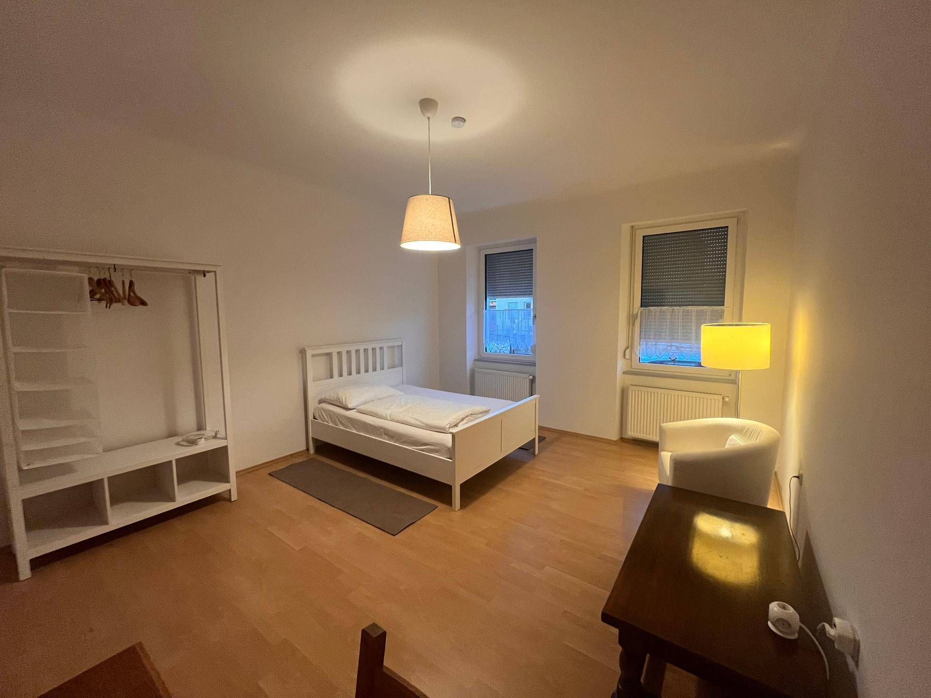 Geräumiges Schlafzimmer mit Doppelbett, offenem Kleiderschrank und zwei Fenstern.