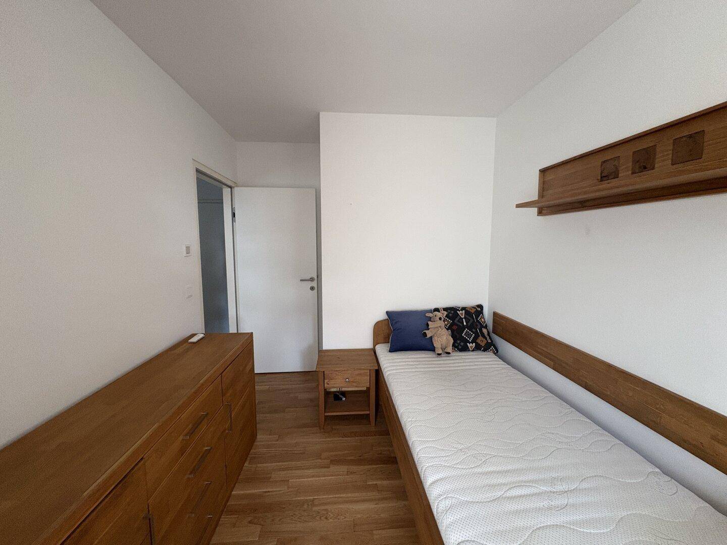 Einfaches Schlafzimmer mit Einzelbett, Holzboden und Holzmöbeln.