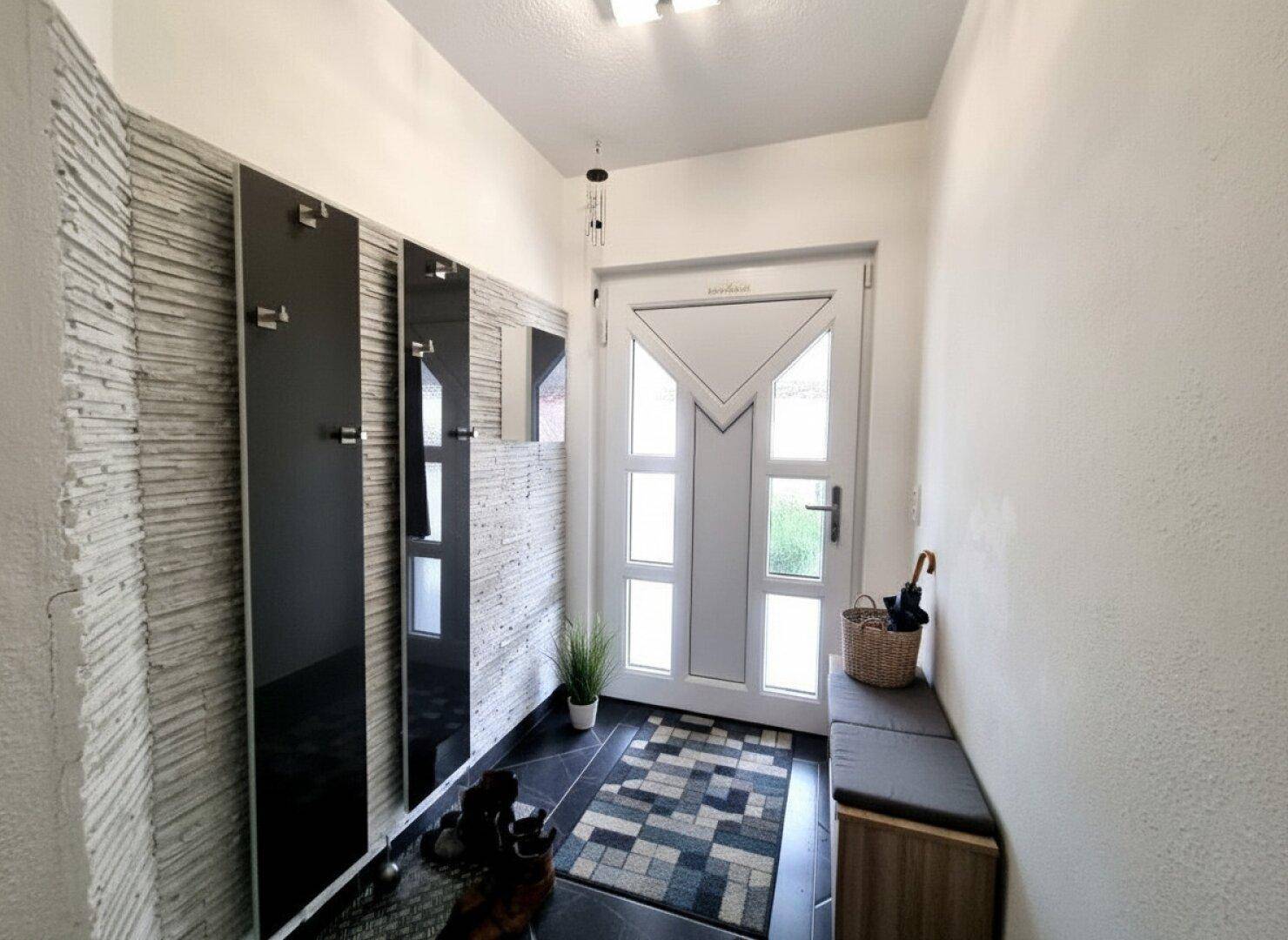 Heller Eingangsbereich mit moderner Haustür, Garderobe und Sitzgelegenheit.