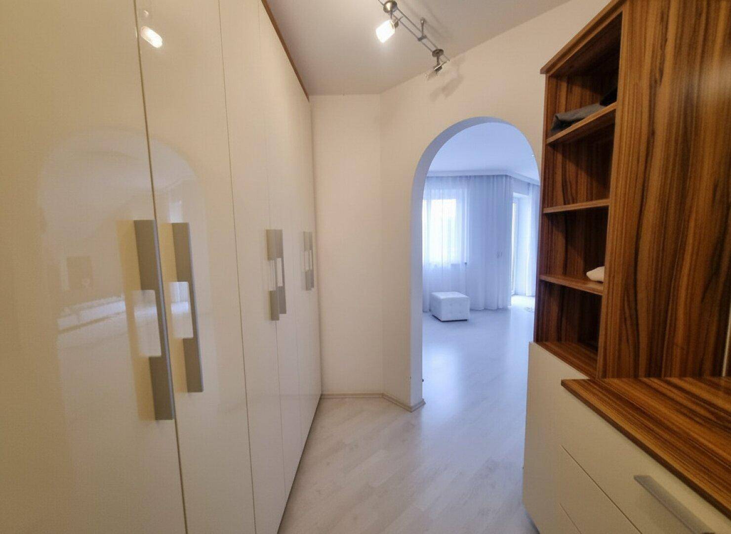 Praktischer Ankleidebereich mit weißen Schränken und Holzregalen, direkt neben dem Schlafzimmer.