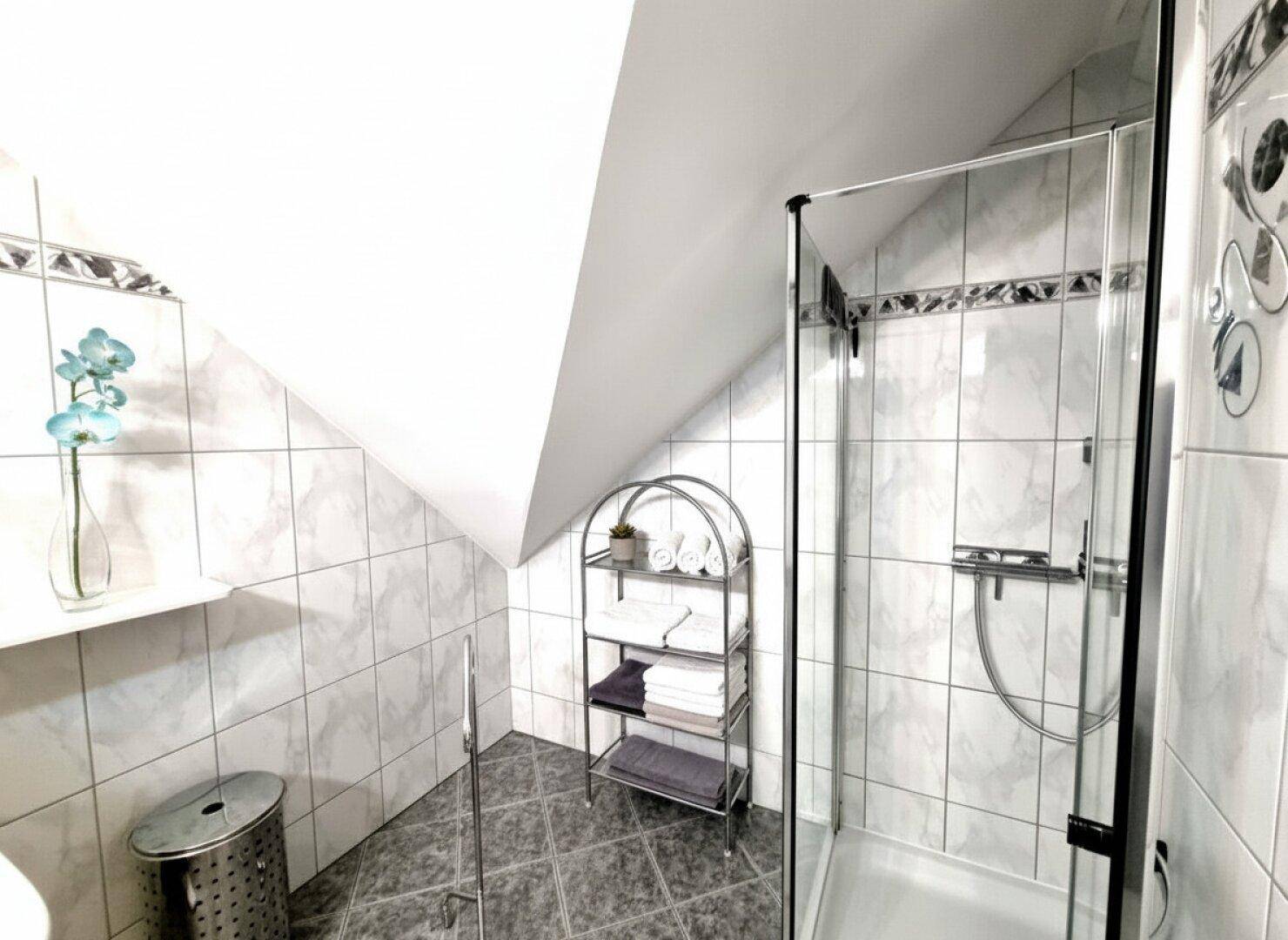 Modernes Badezimmer mit Glasdusche und weißen Fliesen, unter einer Dachschräge gelegen.