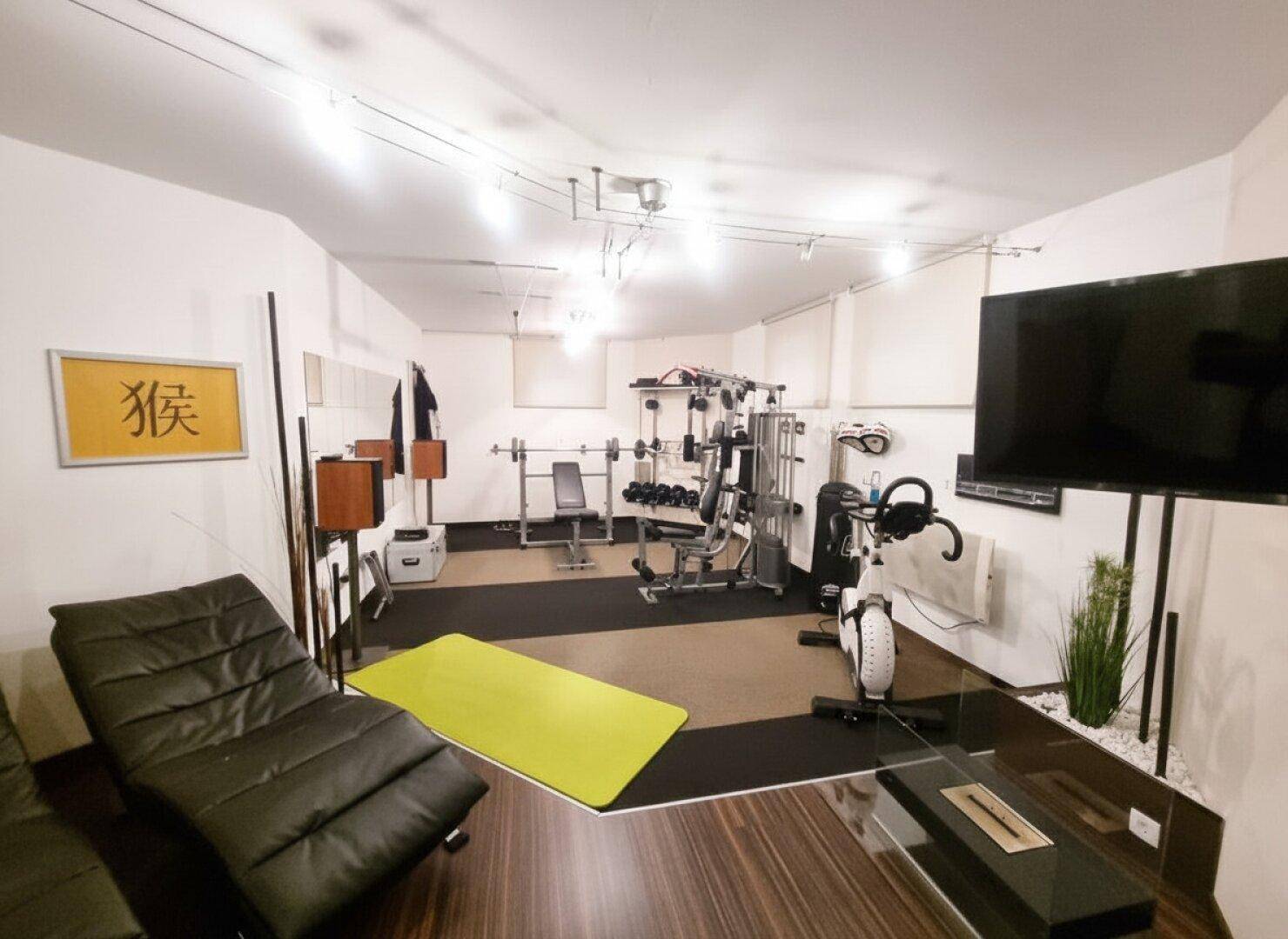 Gut ausgestatteter Fitnessraum mit verschiedenen Geräten und Entspannungsliege, ideal für das Training zu Hause.