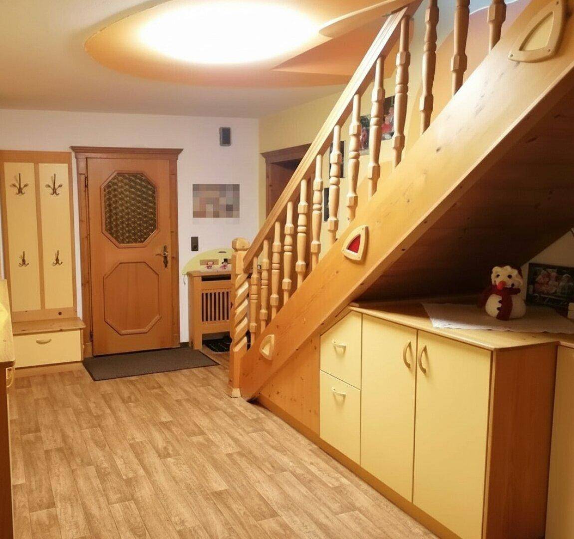 Heller Eingangsbereich mit Holztreppe, integriertem Stauraum und traditioneller Holztür.