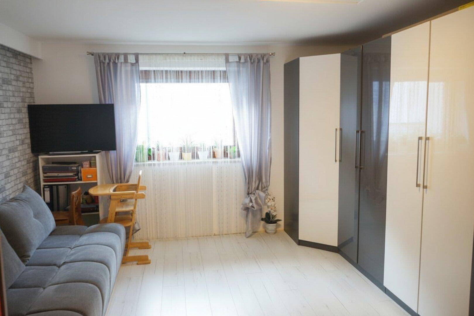 Schlafzimmer mit Sofa, Fernseher und modernen Kleiderschränken in Weiß und Grau.