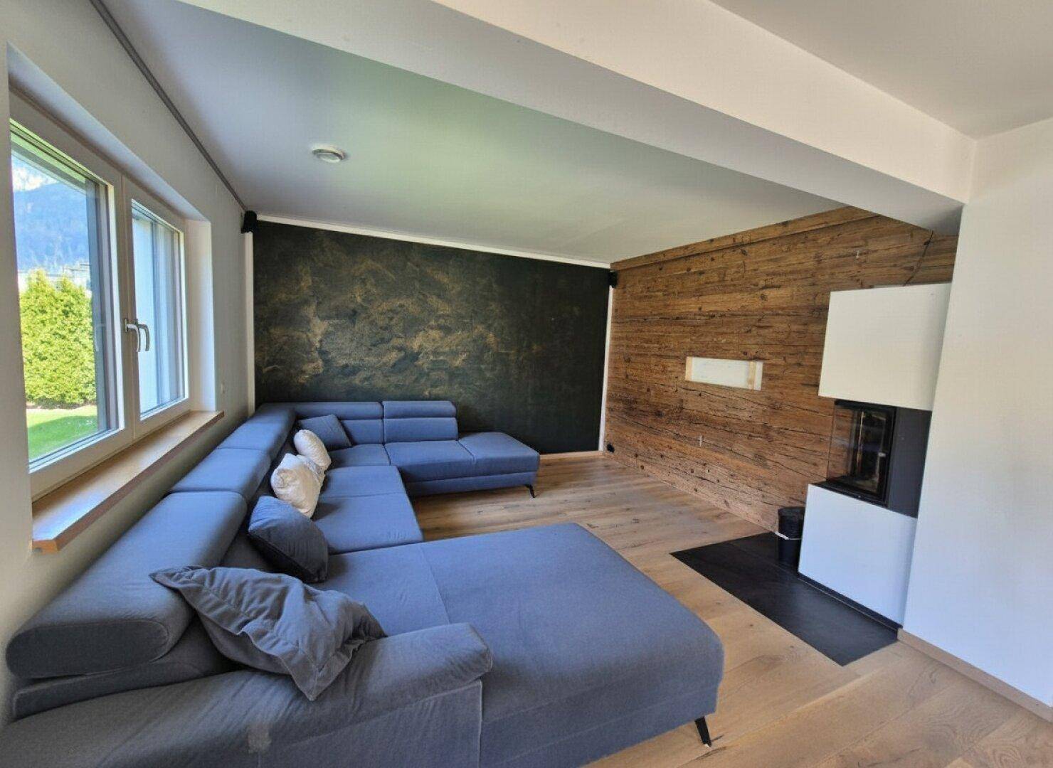 Gemütliches Wohnzimmer mit großem Ecksofa, Holzwand und modernem Kaminofen.