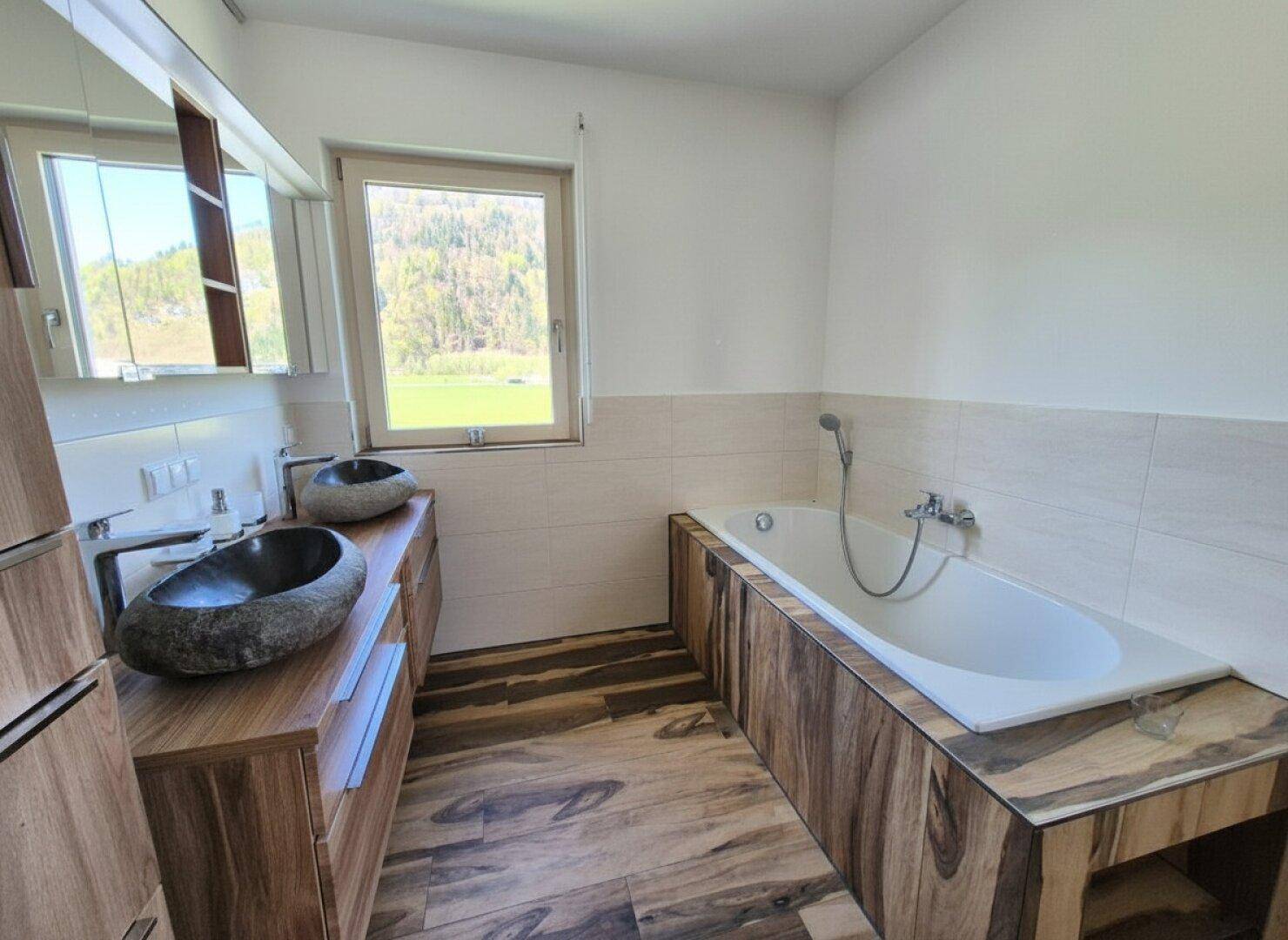 Modernes Badezimmer mit Doppelwaschbecken aus Stein, Badewanne und Holzelementen.