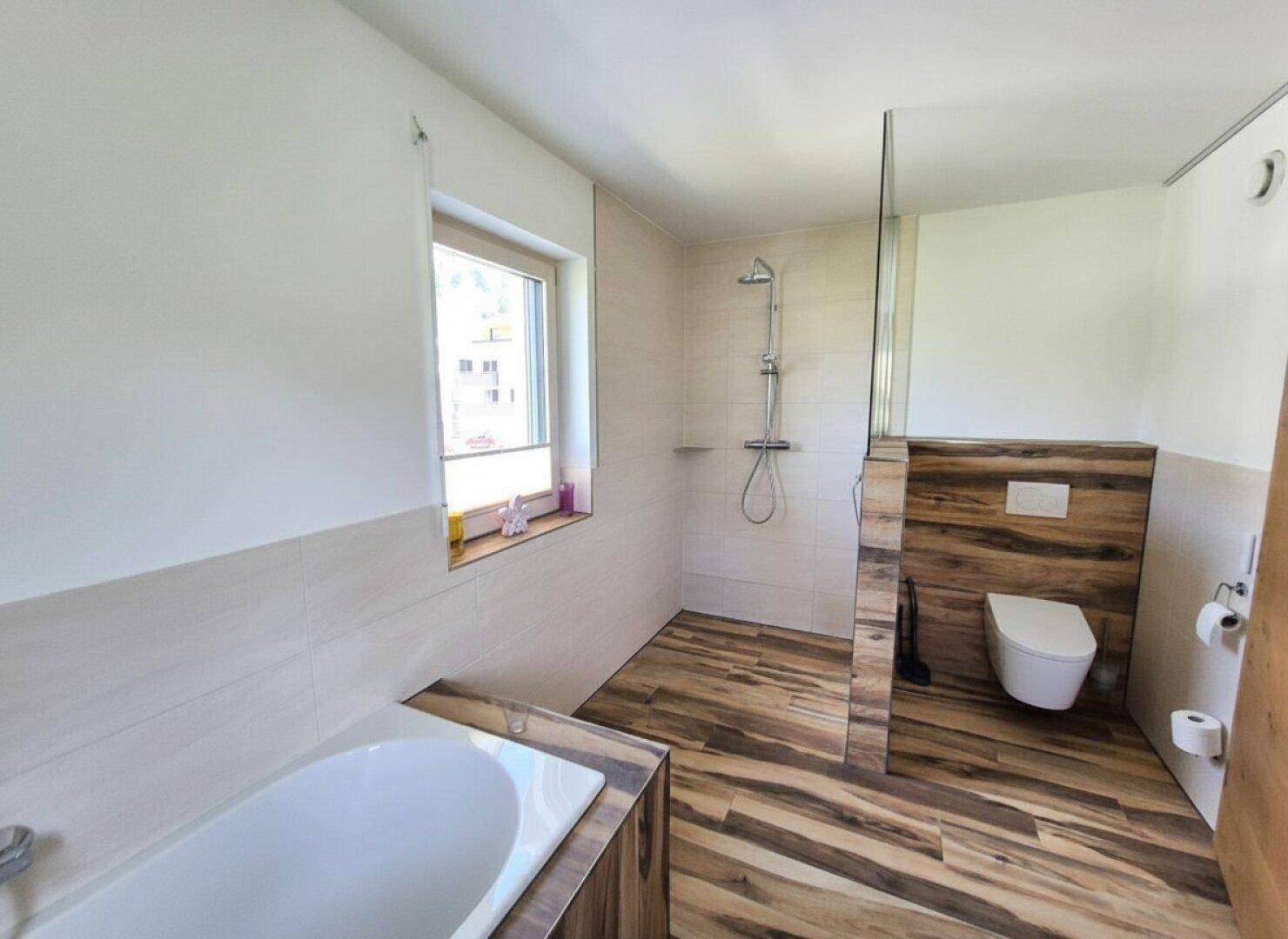 Helles Badezimmer mit Badewanne, Dusche, wandhängendem WC und Holzbodenoptik.