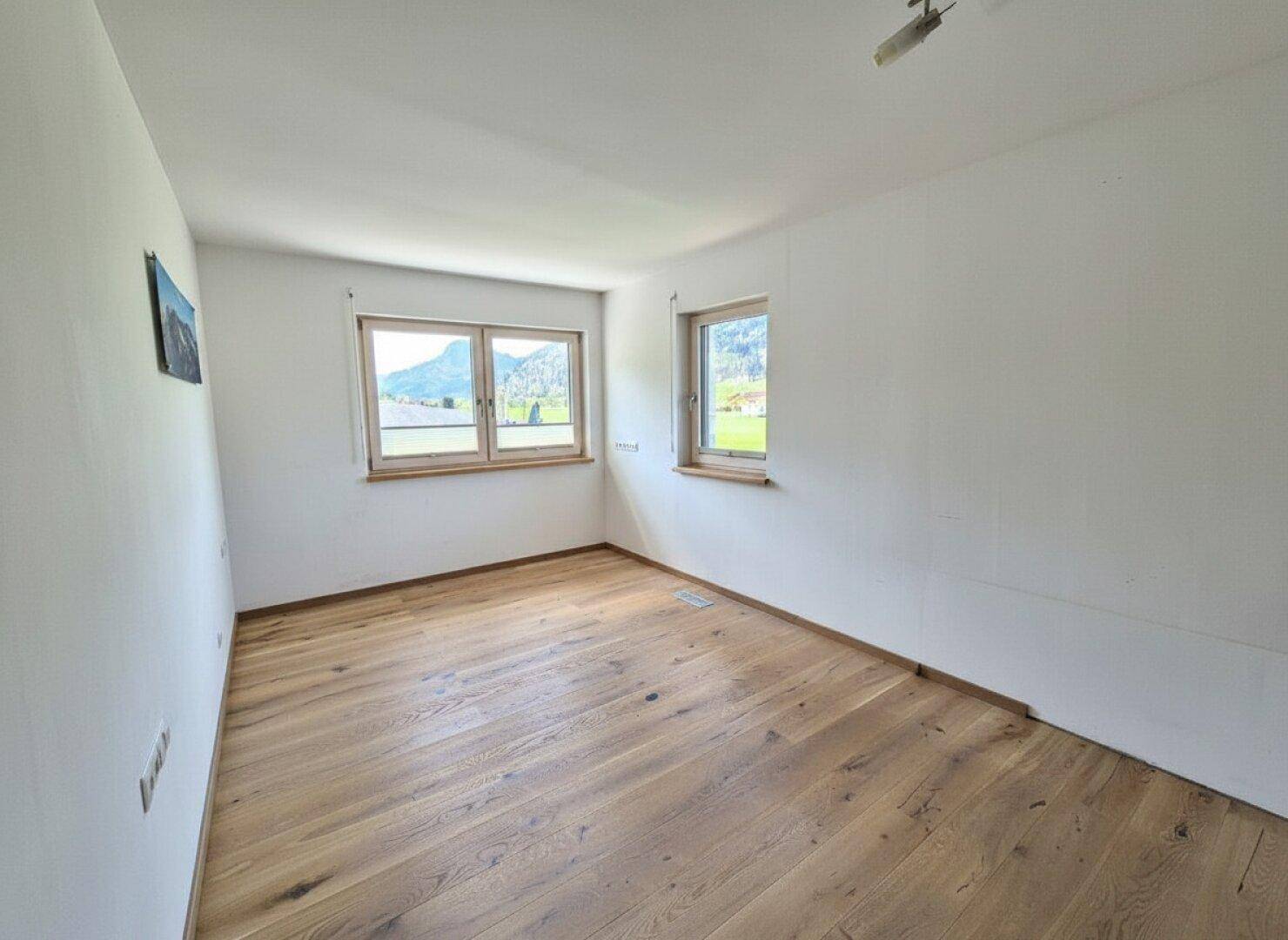 Geräumiges Schlafzimmer mit hellem Parkettboden und Fenstern mit Bergblick.