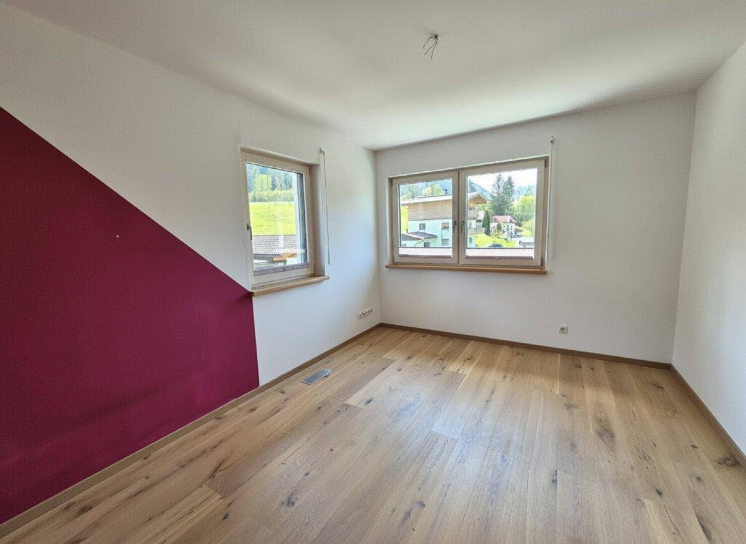Helles Schlafzimmer mit Holzboden, farbiger Akzentwand und Blick ins Grüne.