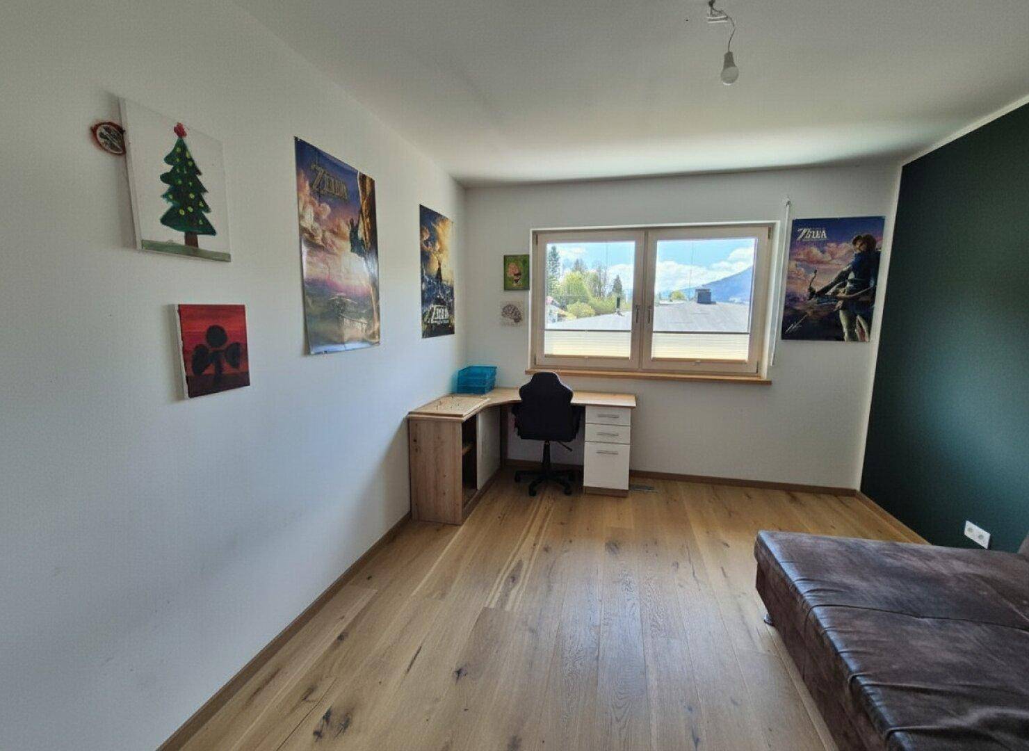 Jugendzimmer mit Schreibtisch, Sofa und großem Fenster mit Ausblick.