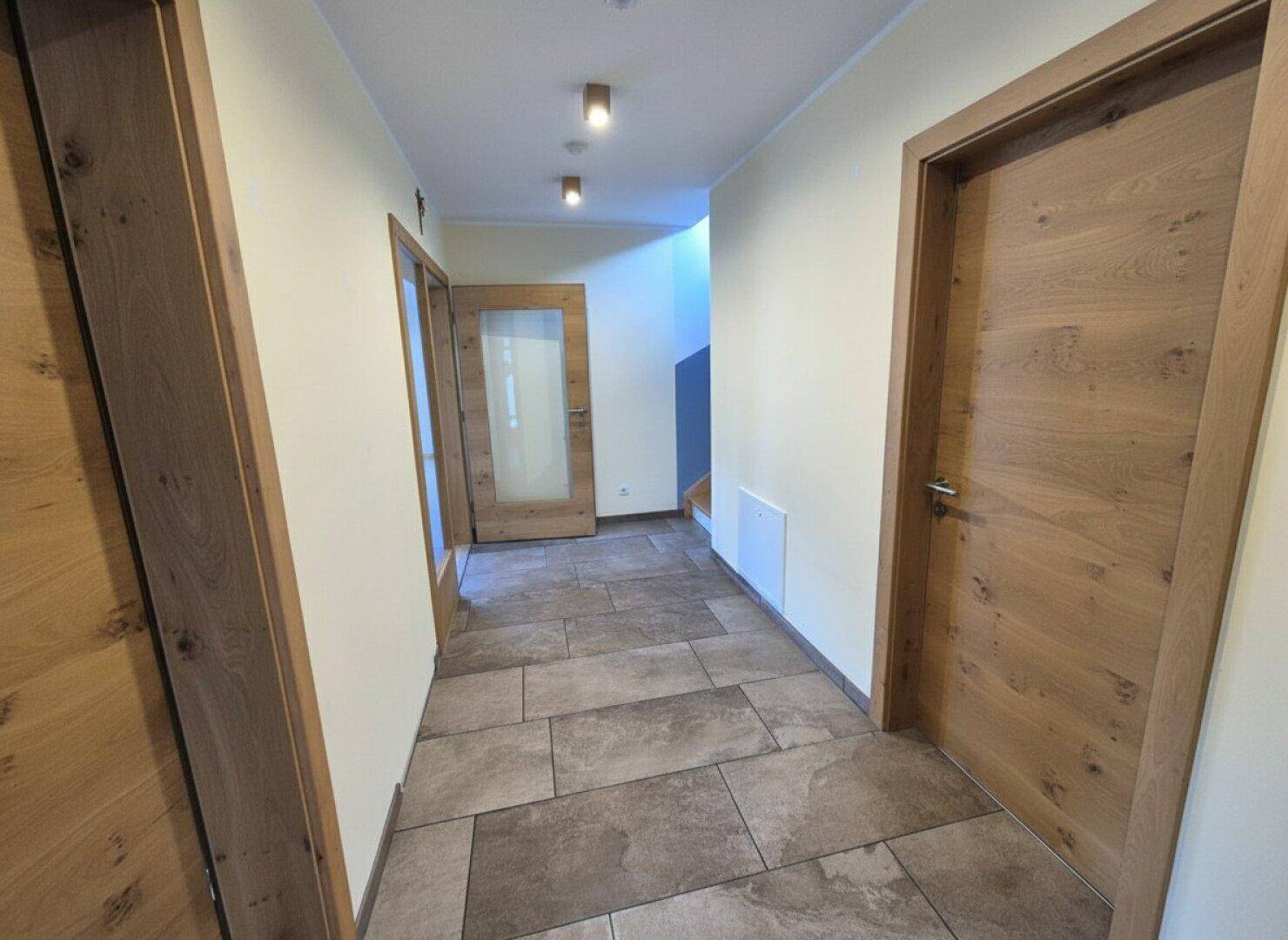 Heller Flur mit Fliesenboden und modernen Holztüren.