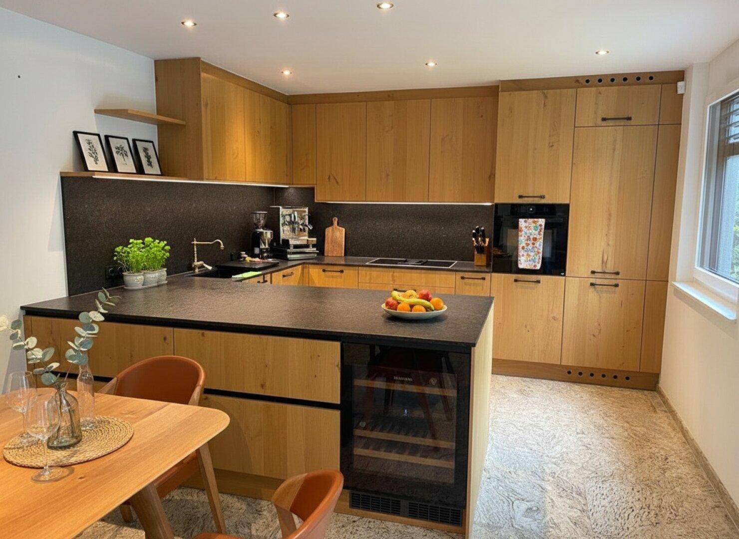 Moderne Holzküche mit dunkler Arbeitsplatte, Kücheninsel und integriertem Weinkühler.