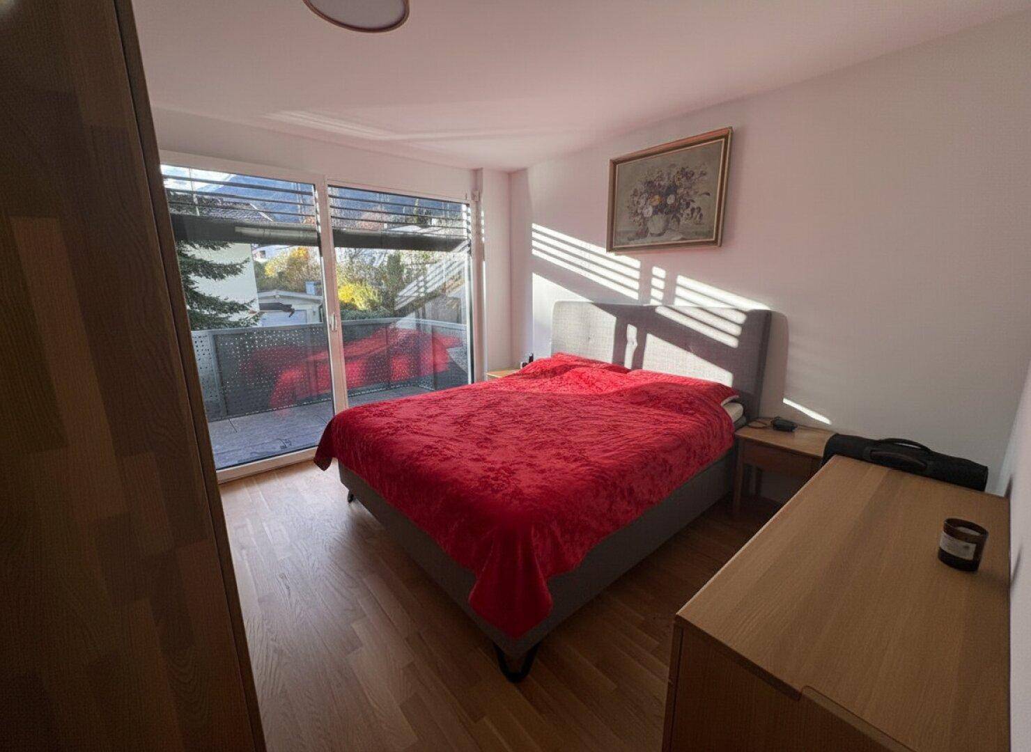 Helles Schlafzimmer mit Holzboden, Doppelbett und Zugang zum Balkon.