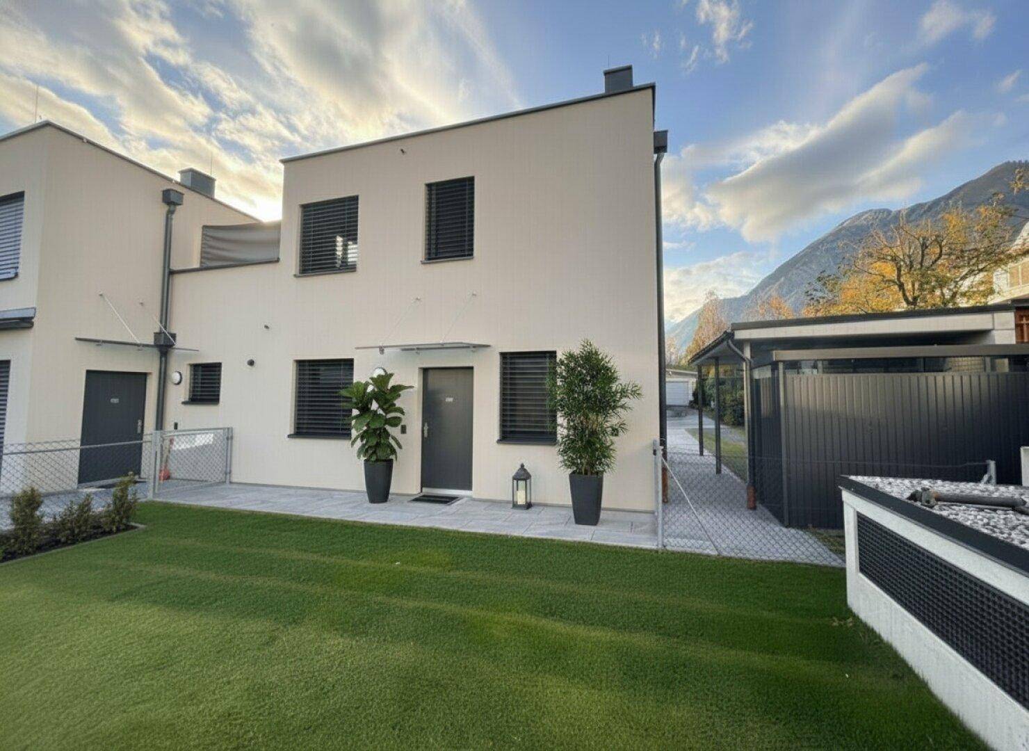 Vorderansicht eines modernen Hauses mit gepflegtem Rasen und dekorativen Pflanzen am Eingang.