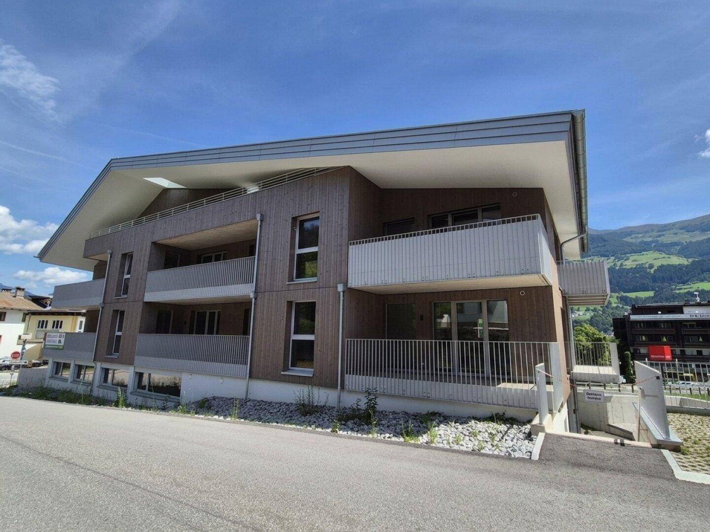Neubau mit Holzfassade, mehreren Balkonen und Blick auf die umliegende Berglandschaft.