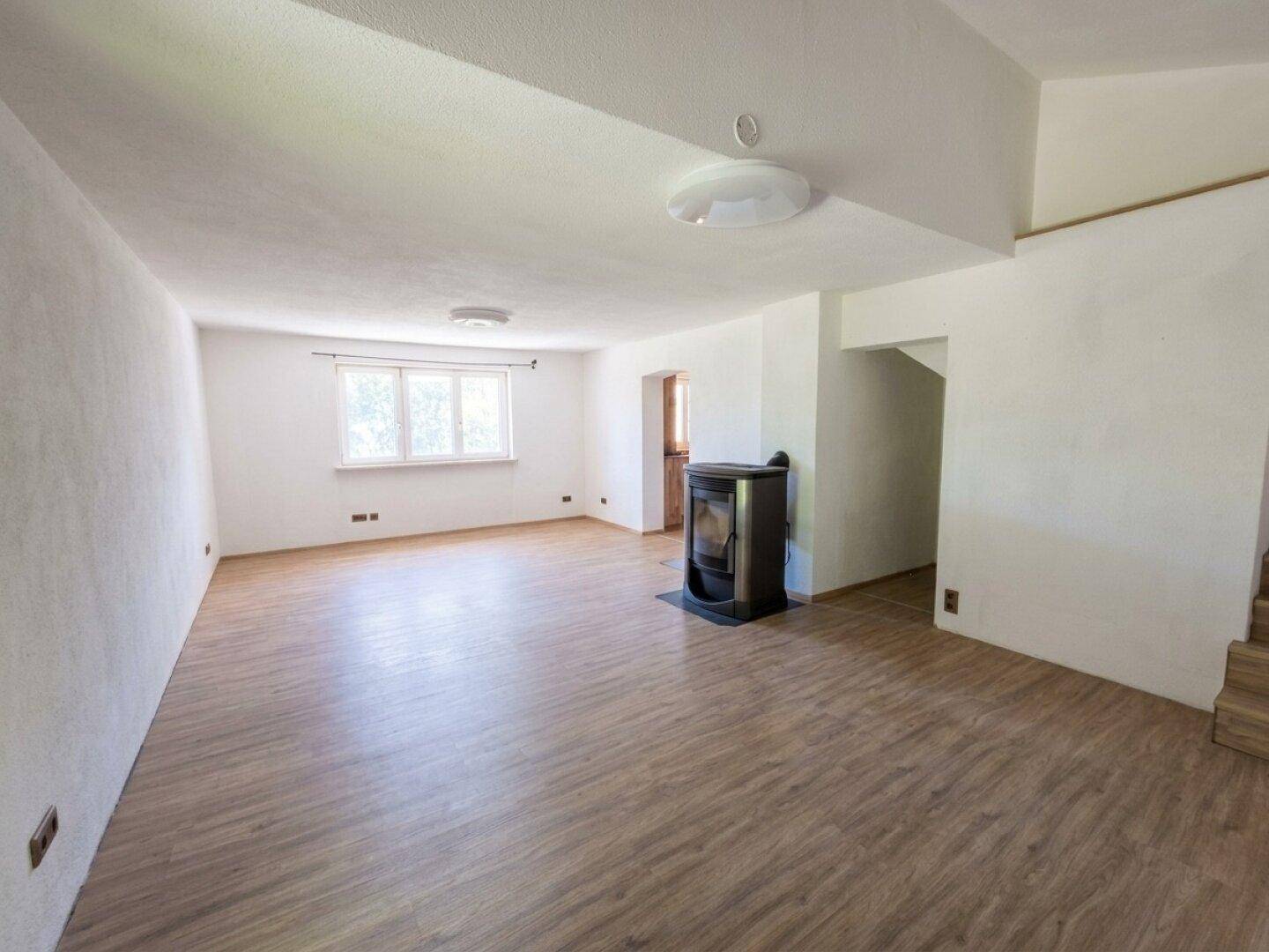 Geräumiges Wohnzimmer mit Laminatboden, weiß gestrichenen Wänden und einem modernen Kaminofen.