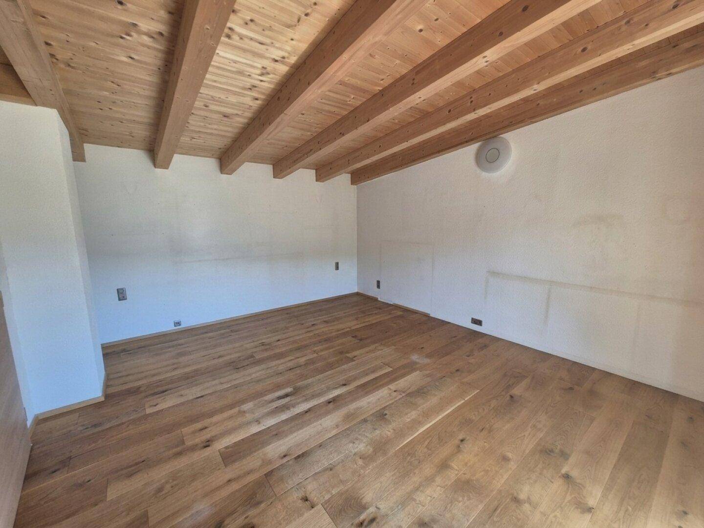 Helles Zimmer mit Holzbalkendecke und neuem Holzboden, bereit zur individuellen Gestaltung.