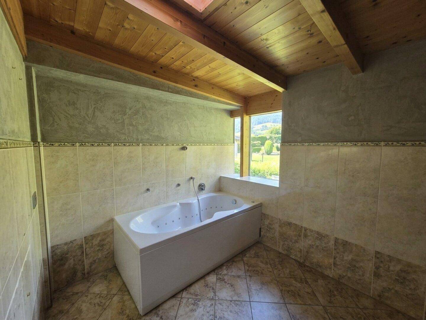 Badezimmer mit Eckbadewanne, Fliesen und Blick auf die grüne Umgebung.