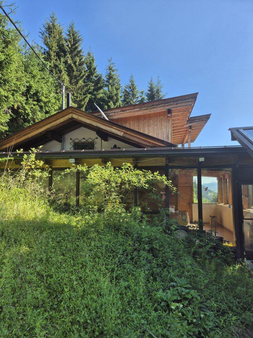 Seitenansicht des Hauses mit üppigem Grün und Blick auf die umliegende Berglandschaft.