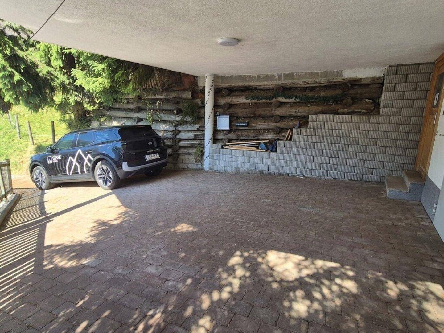 Überdachter Stellplatz mit gepflastertem Boden und Holzwand im Hintergrund.