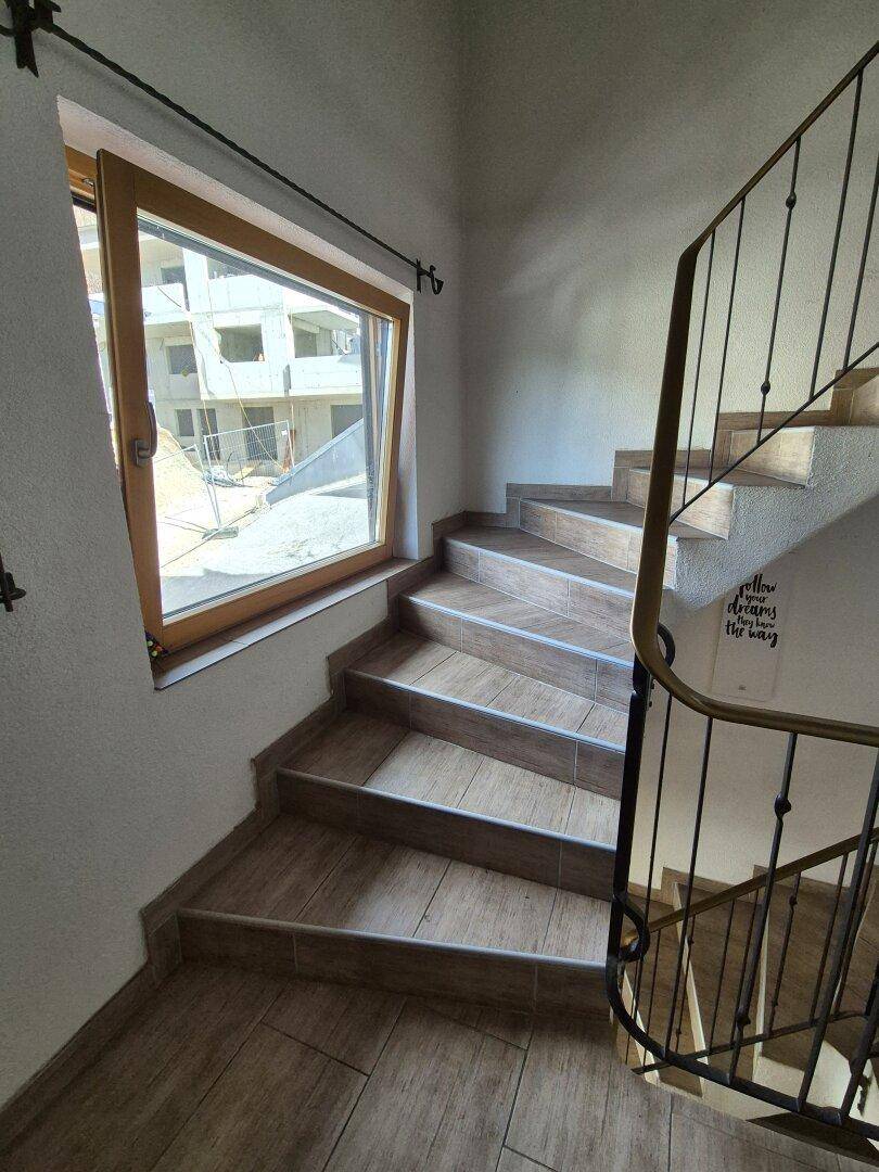 Wendeltreppe mit Holzstufen und Metallgeländer, beleuchtet durch ein großes Fenster.