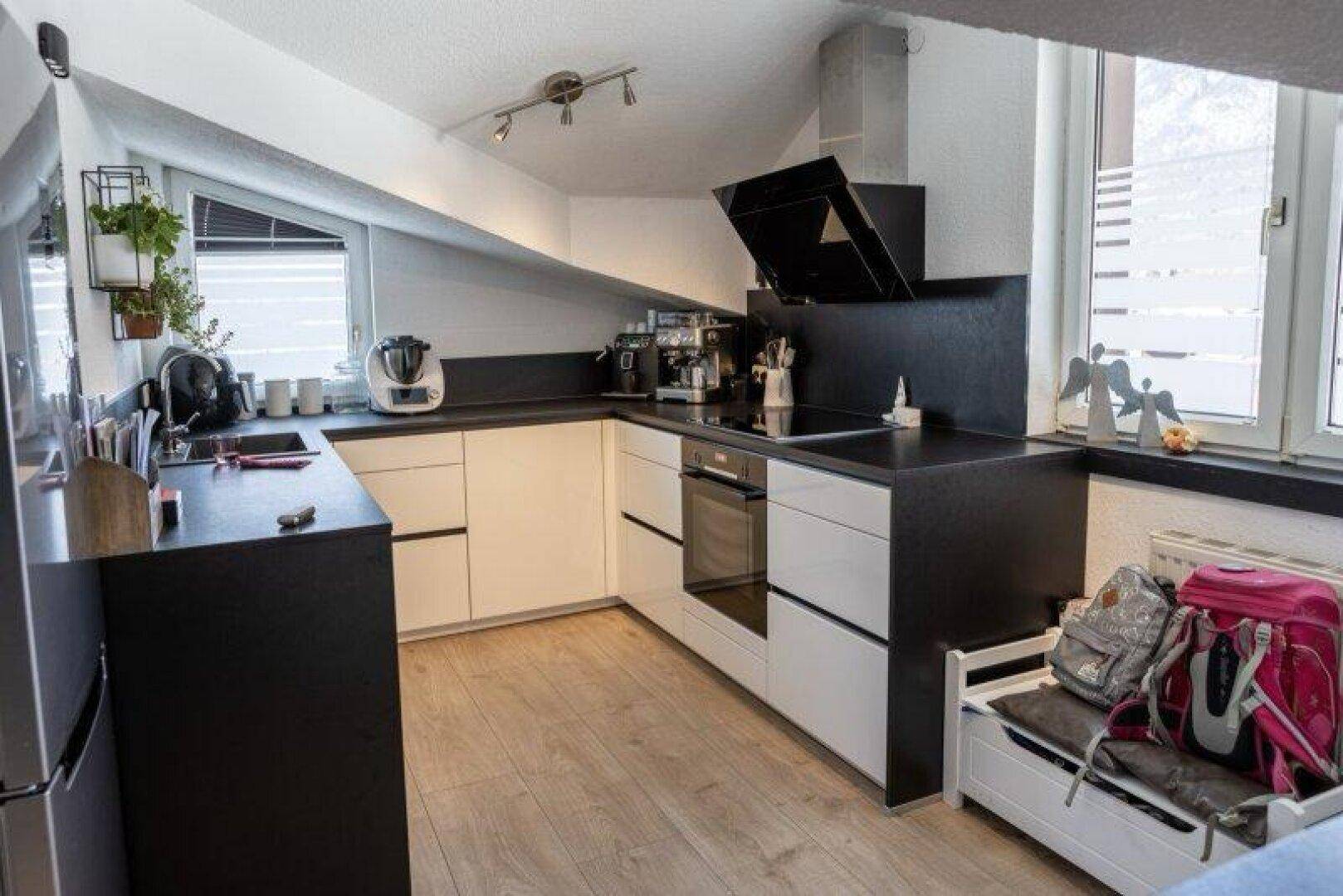 Moderne Küche mit schwarzen Arbeitsplatten, weißen Schränken und Dachschrägenfenstern.