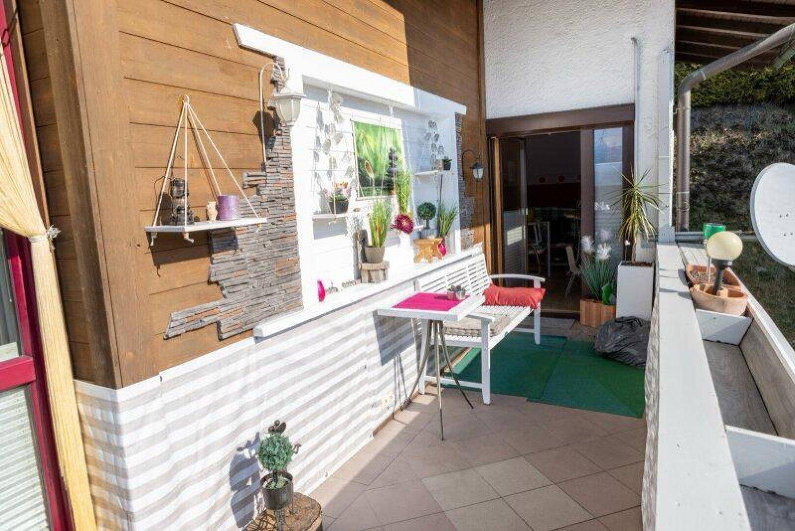 Gemütlicher Balkon mit Holzwand, Sitzgelegenheiten und Blick ins Grüne.