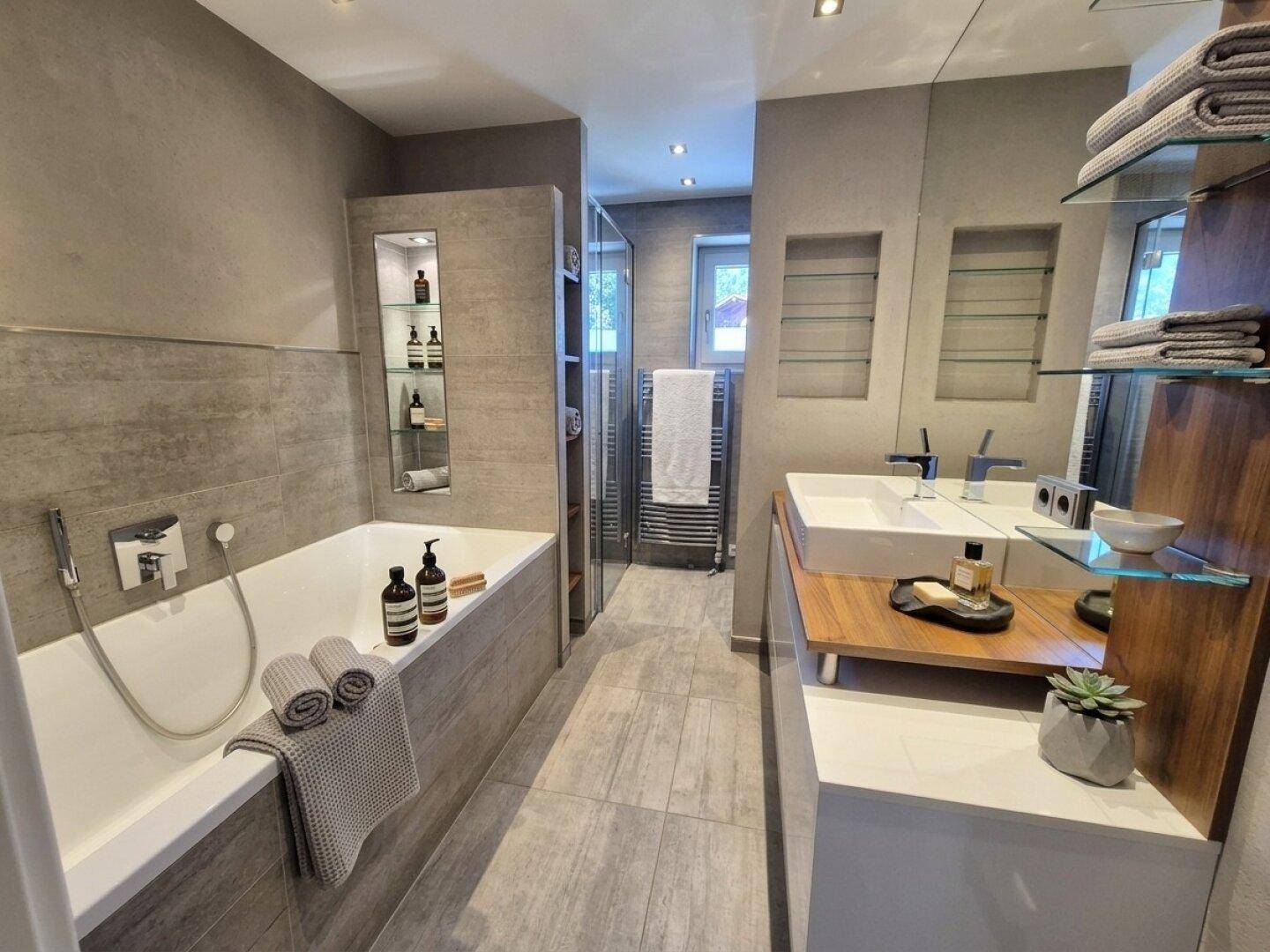 Modernes Badezimmer mit Badewanne, Dusche, Doppelwaschbecken und grauen Fliesen.