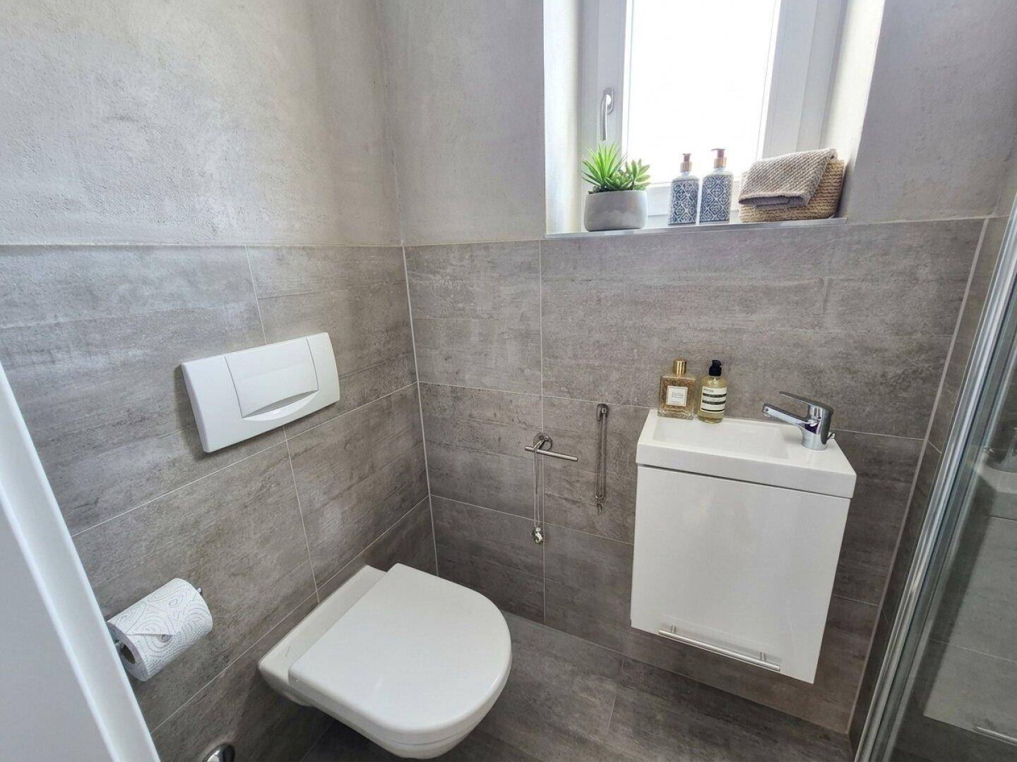 Kleines Gäste-WC mit Fenster, Wand-WC und modernem Waschbecken.