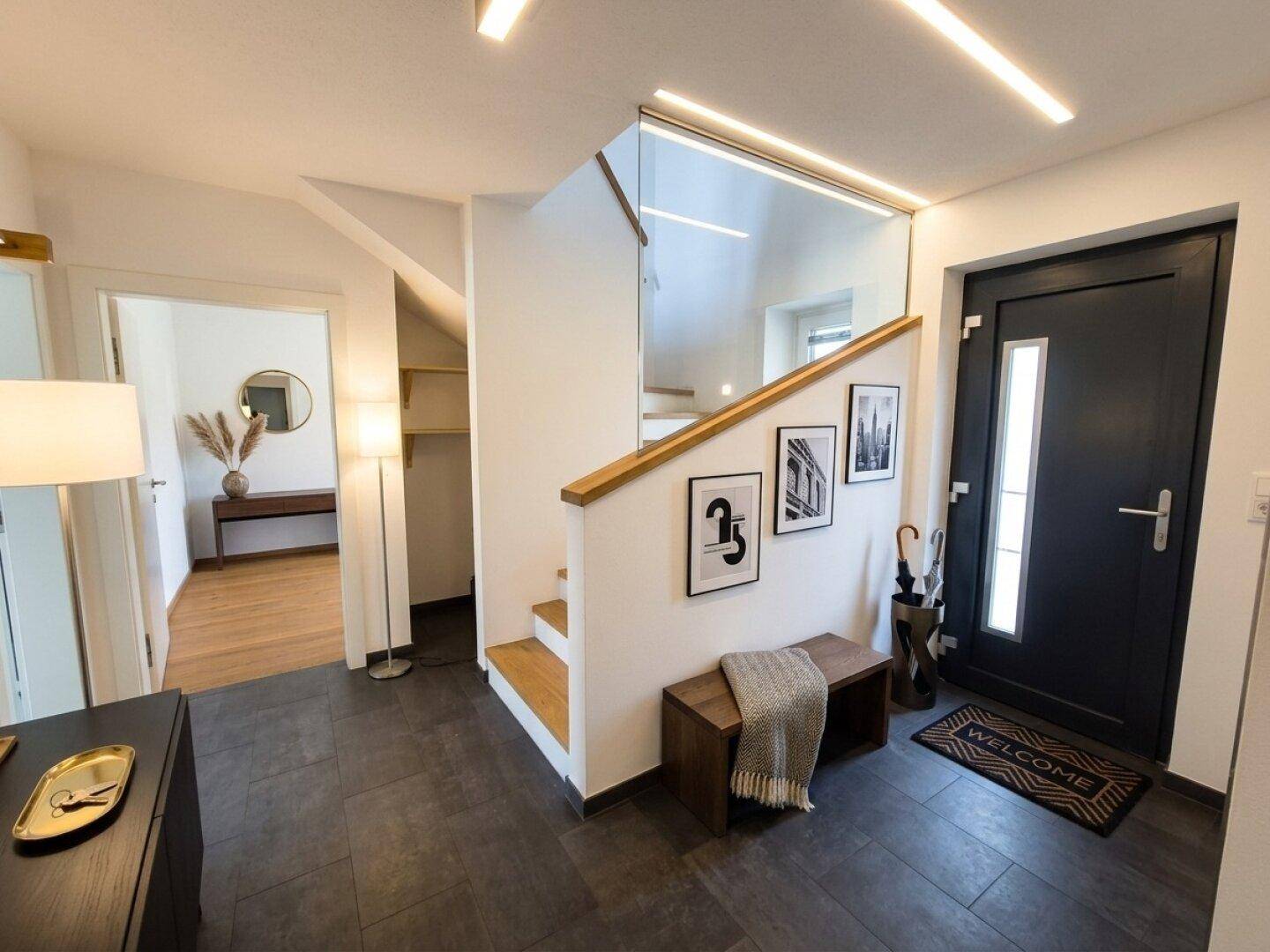 Heller Eingangsbereich mit dunklen Fliesen, moderner Treppe und Glasgeländer.