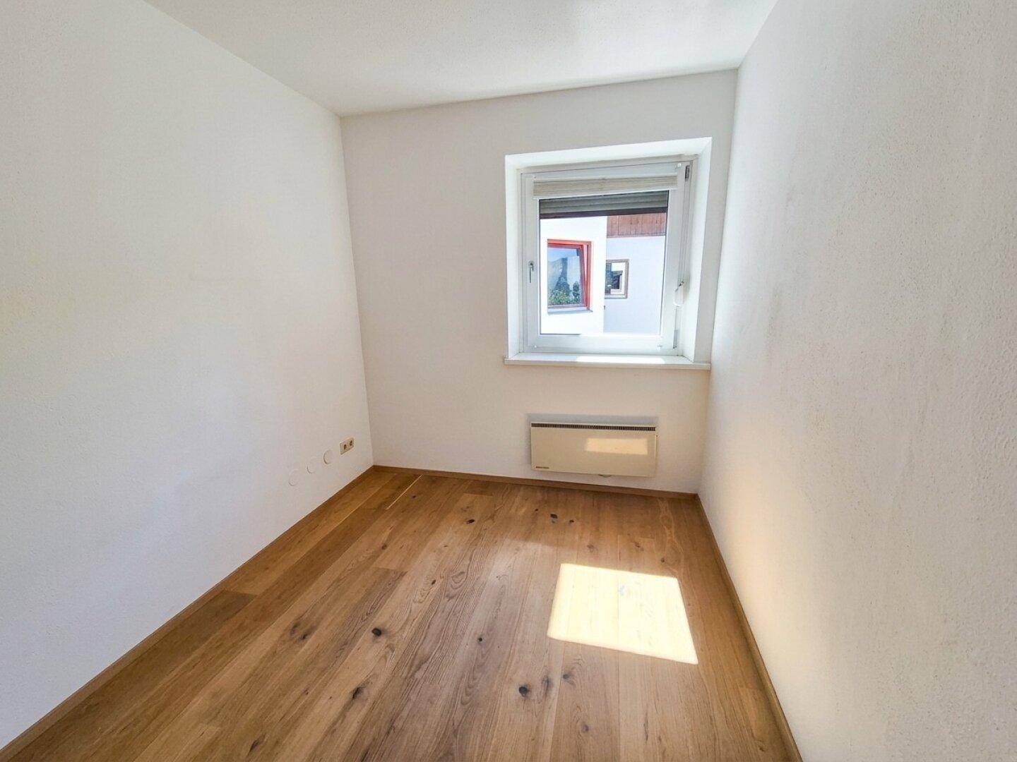 Kleines helles Zimmer mit Holzboden und einem Fenster.