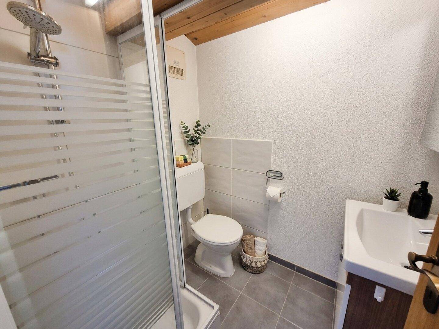 Badezimmer mit Dusche, WC, Waschbecken und Holzbalken an der Decke.