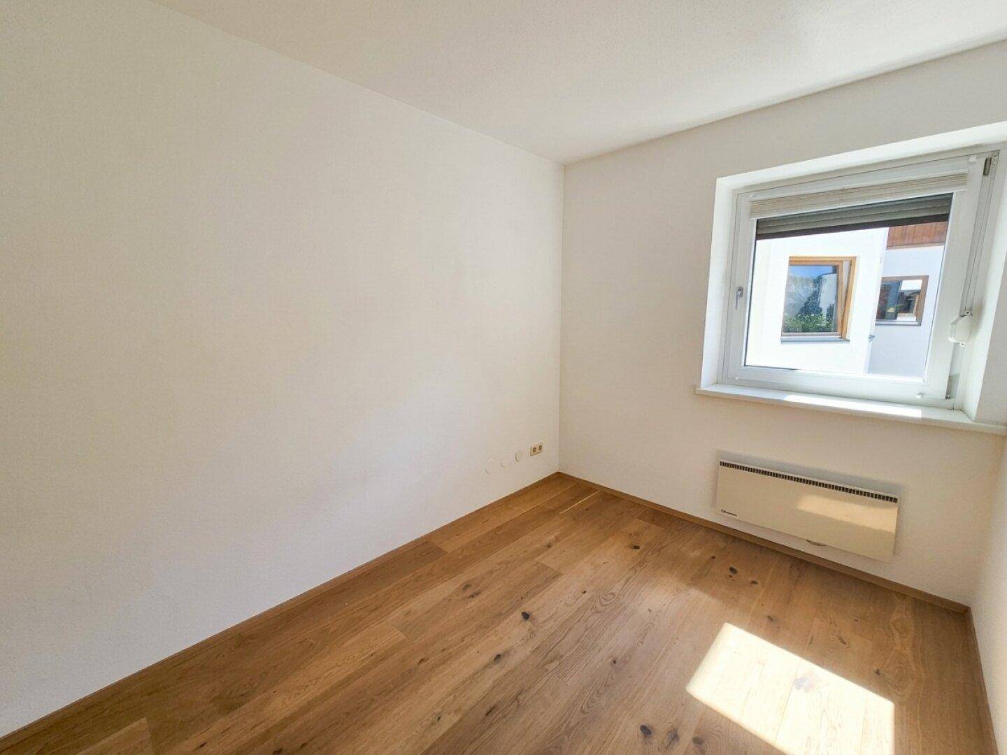 Helles leeres Zimmer mit Holzboden und einem Fenster.