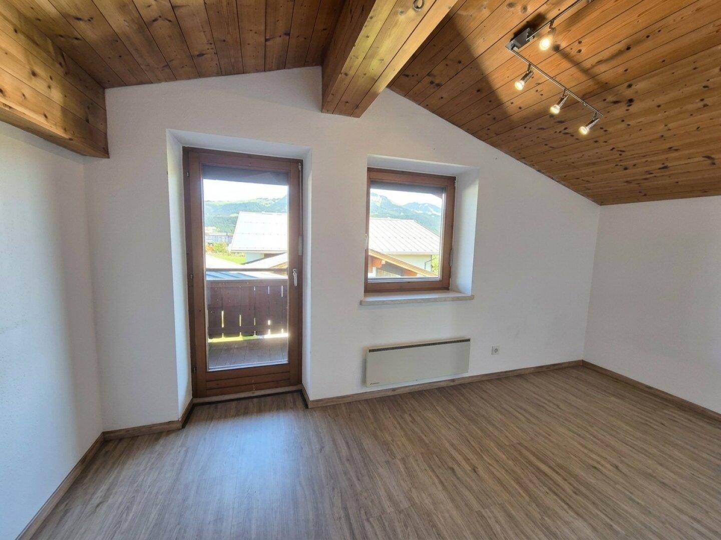 Helles Zimmer im Dachgeschoss mit Holzboden, Balkonzugang und schräger Decke.
