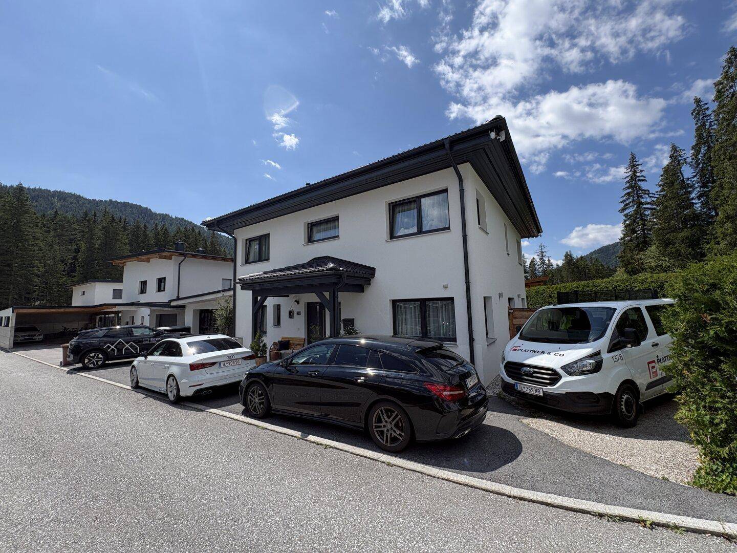 Modernes Einfamilienhaus mit mehreren Parkplätzen und malerischem Bergblick.