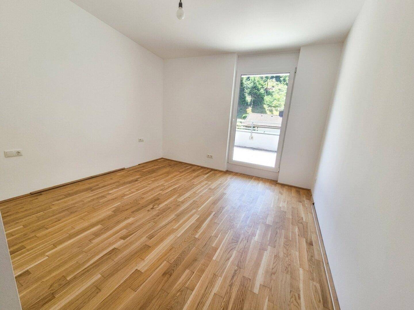 Leeres Zimmer mit hellem Holzparkett und Zugang zu einem Außenbereich.