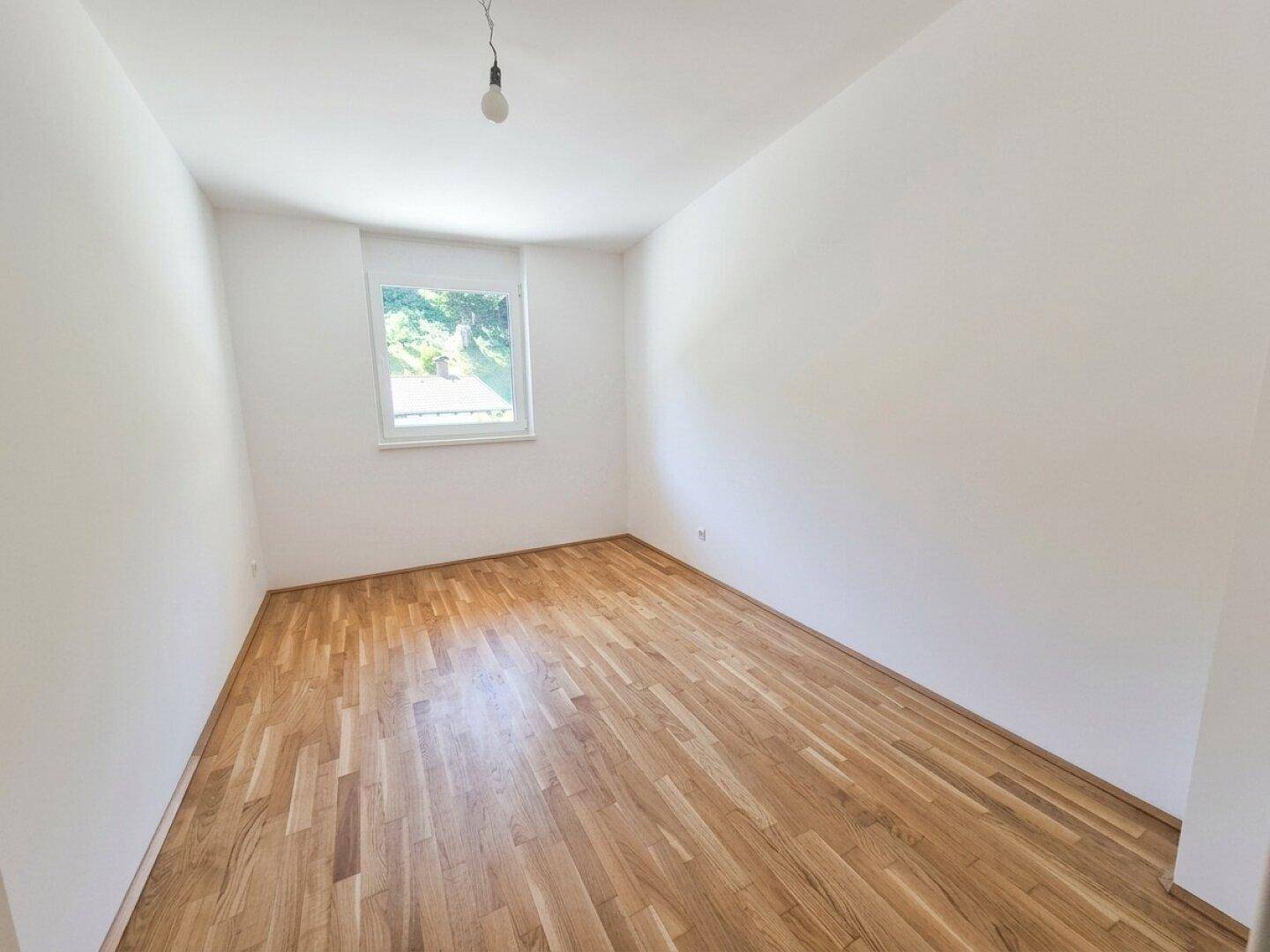 Helles Zimmer mit Holzparkettboden und einem Fenster, bereit zur individuellen Gestaltung.