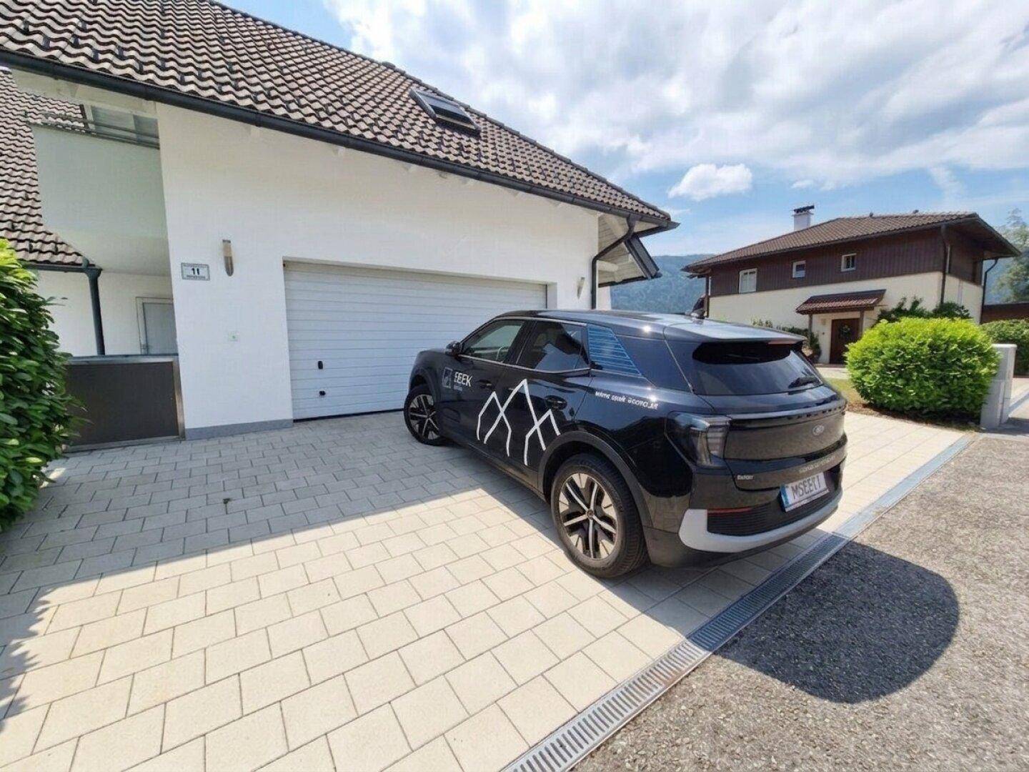 Hauseingang mit Garage und gepflasterter Auffahrt, ein modernes Auto ist geparkt.