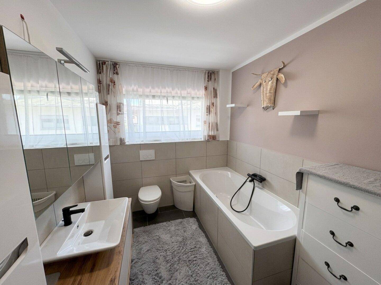 Badezimmer mit Badewanne, modernem Waschtisch und Fenster für Tageslicht.