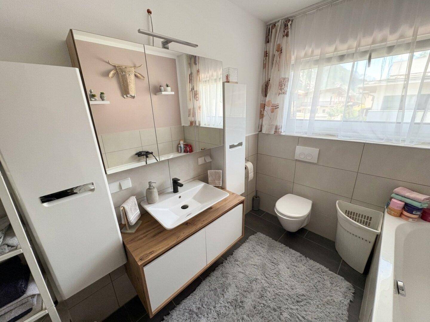 Modernes Badezimmer mit Einzelwaschbecken, WC und Fenster für natürliche Belüftung.