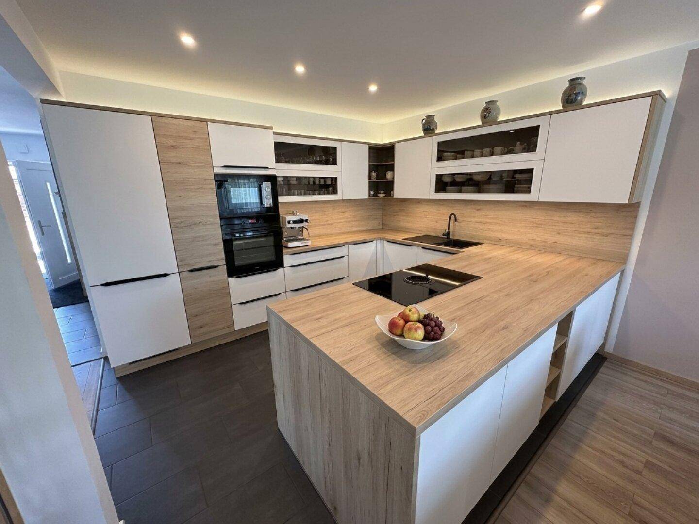 Moderne Einbauküche mit Kücheninsel, integrierten Geräten und hellen Holz- und Weißfronten.