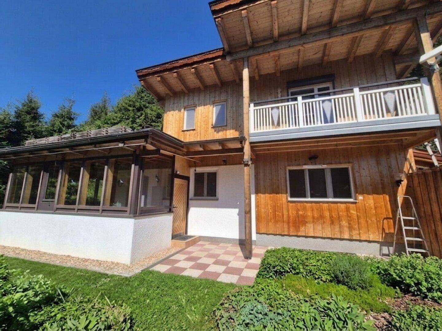 Charmantes Holzhaus mit Balkon, Wintergarten und kleiner gepflasterter Terrasse.