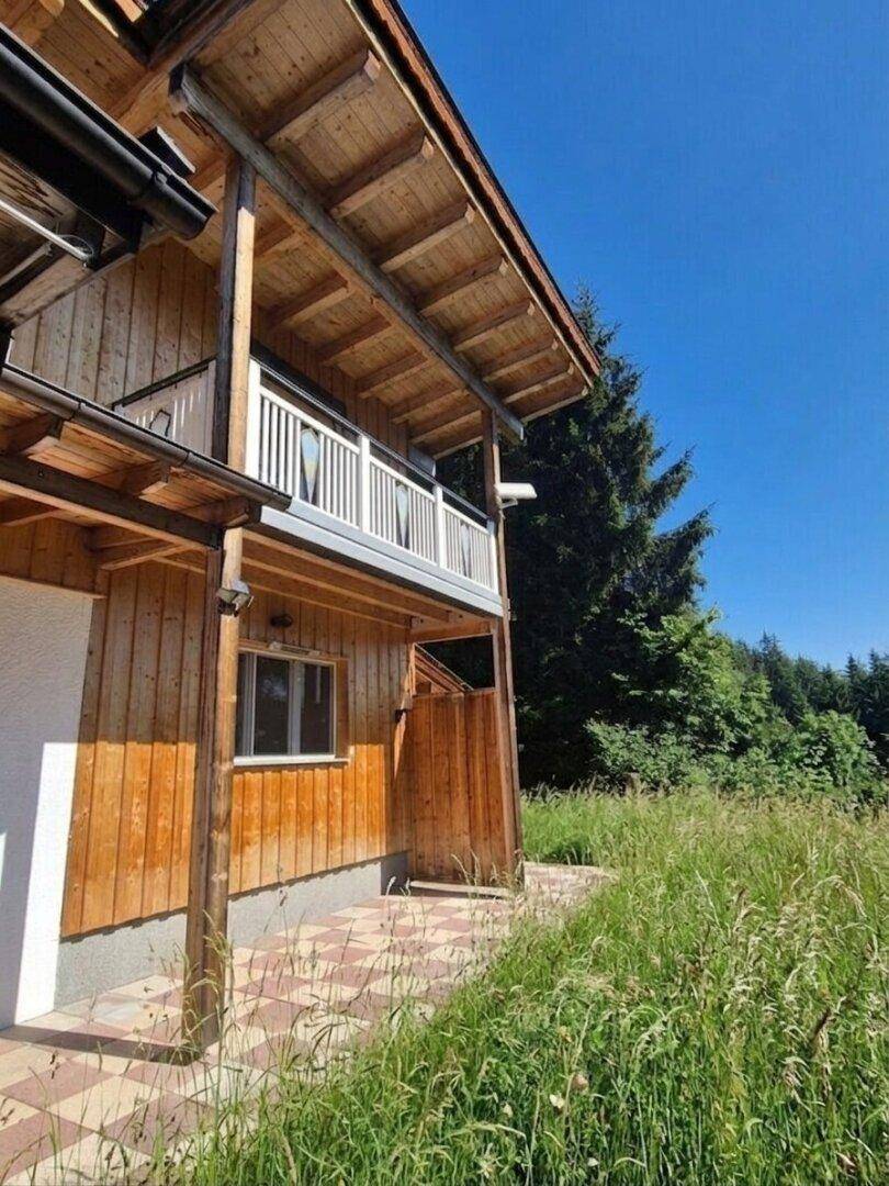 Seitenansicht des Holzhauses mit Balkon und weitem Blick ins Grüne.