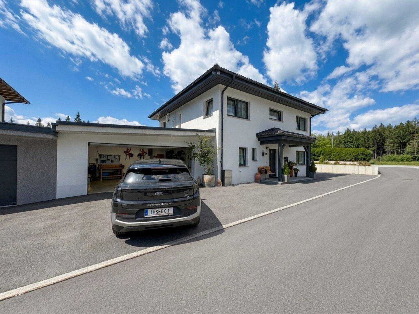 Modernes Einfamilienhaus mit weißer Fassade, großem Garagenbereich und Blick ins Grüne.