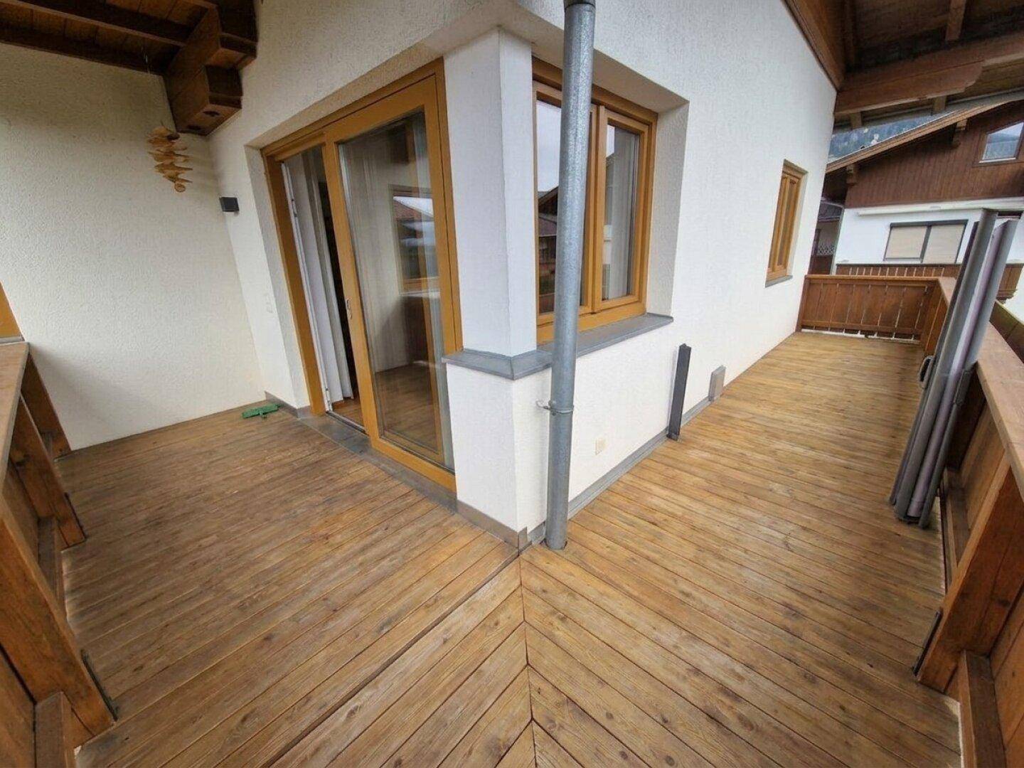 Geräumiger Holzbalkon mit Zugang zum Innenbereich und Blick auf die Umgebung.