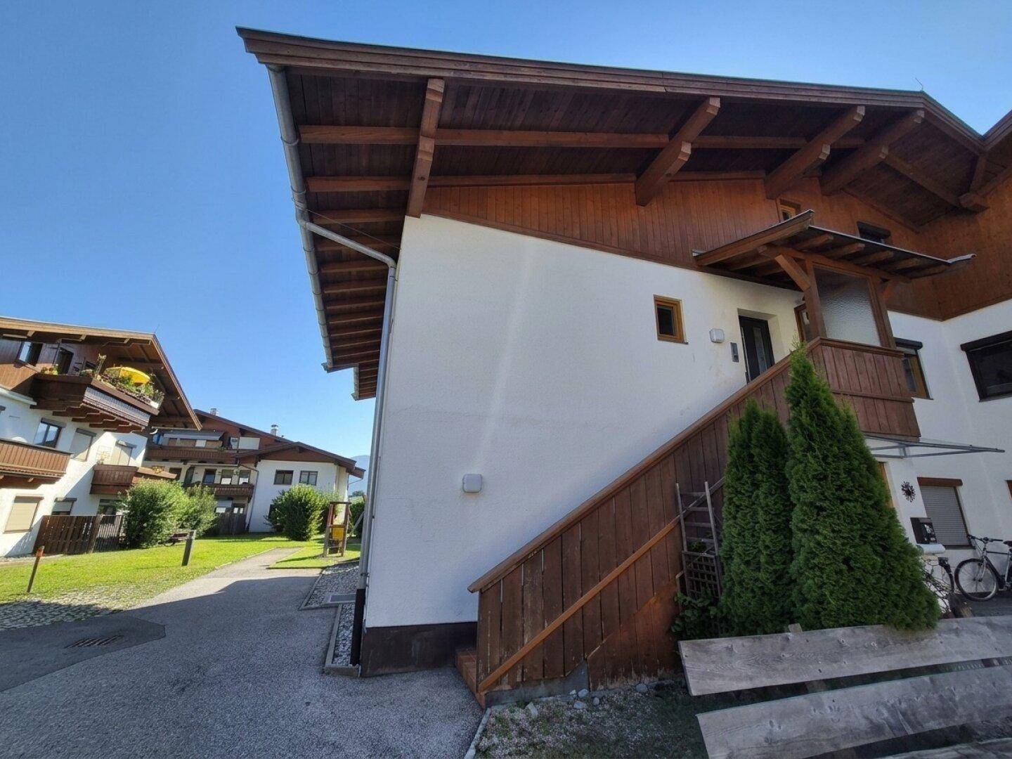 Außenansicht eines modernen Gebäudes mit Holzfassade, Außentreppe und gepflegter Grünanlage.