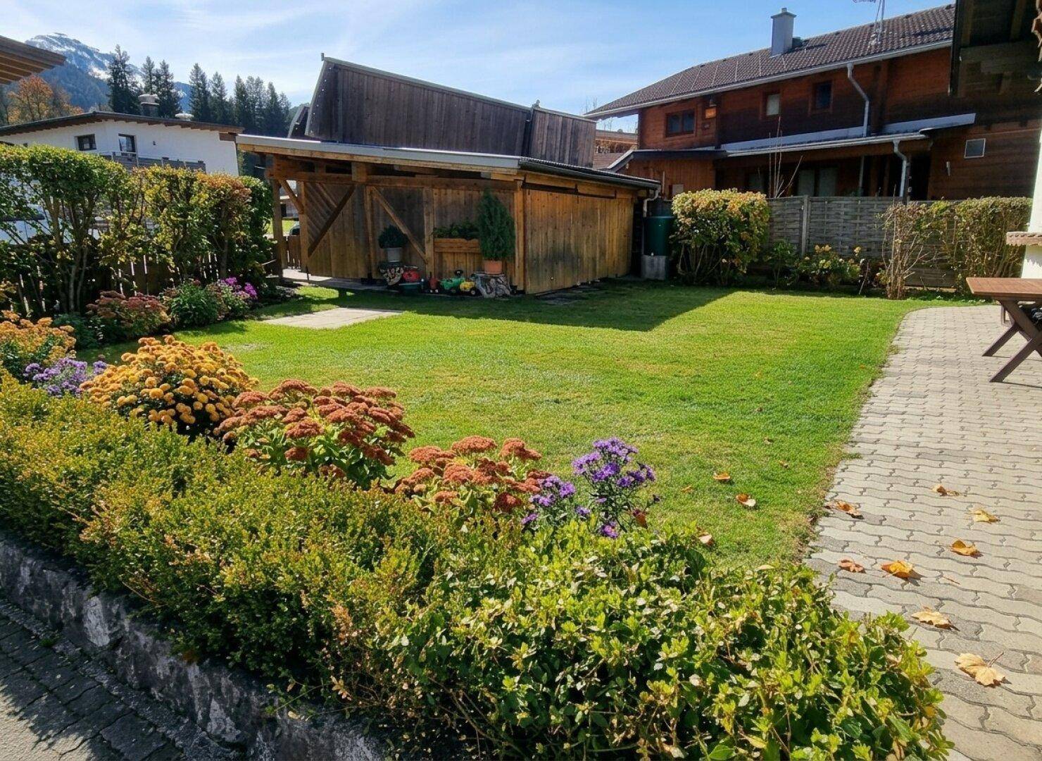 Gepflegter Gartenbereich mit Rasenfläche, blühenden Sträuchern und einem Holzschuppen.